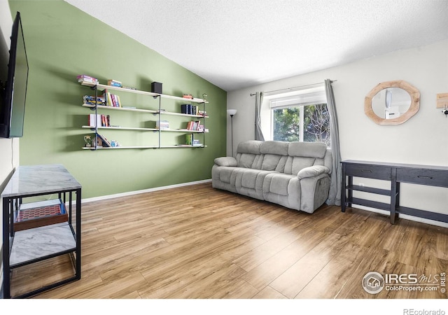 living room featuring vaulted ceiling, wood finished floors, baseboards, and a textured ceiling