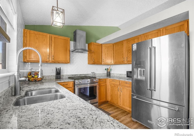 kitchen with high end appliances, light wood-type flooring, a sink, wall chimney exhaust hood, and tasteful backsplash