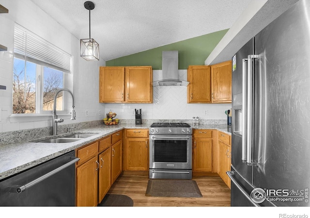 kitchen featuring a sink, wood finished floors, stainless steel appliances, wall chimney range hood, and vaulted ceiling