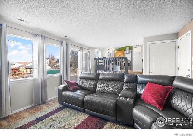 living room featuring visible vents, a healthy amount of sunlight, a textured ceiling, and wood finished floors