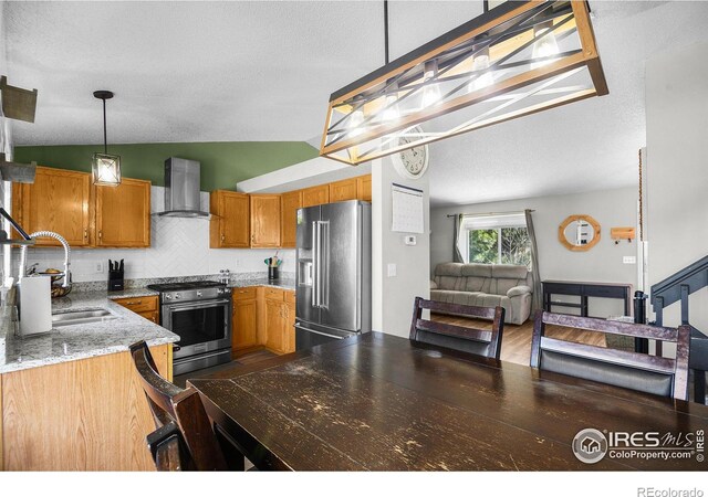 kitchen with a sink, decorative backsplash, appliances with stainless steel finishes, wall chimney exhaust hood, and brown cabinets