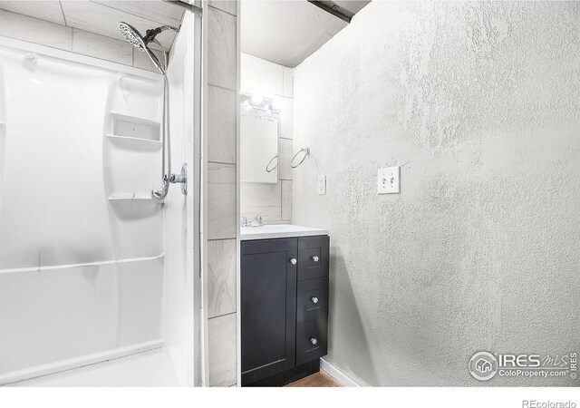 full bath with vanity, a textured wall, and a stall shower