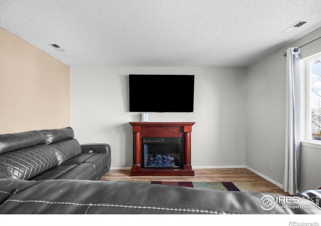 living room with wood finished floors, baseboards, visible vents, a fireplace, and a textured ceiling