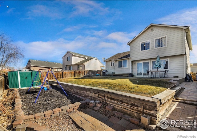 back of house featuring a playground, fence, a yard, an outbuilding, and a storage unit