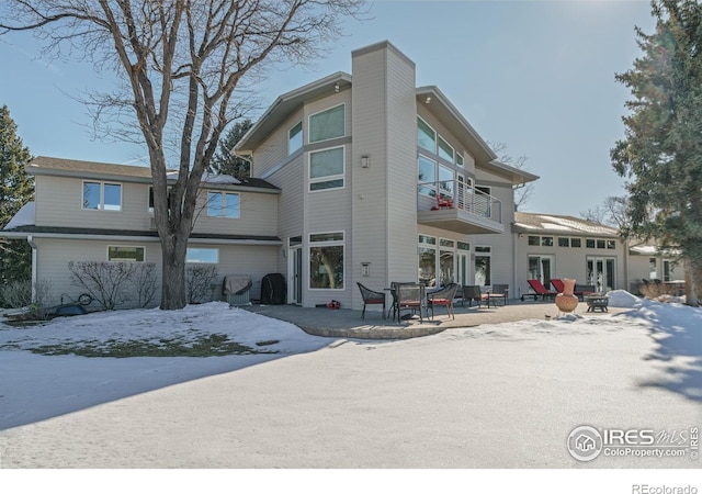 snow covered rear of property featuring a patio and a balcony