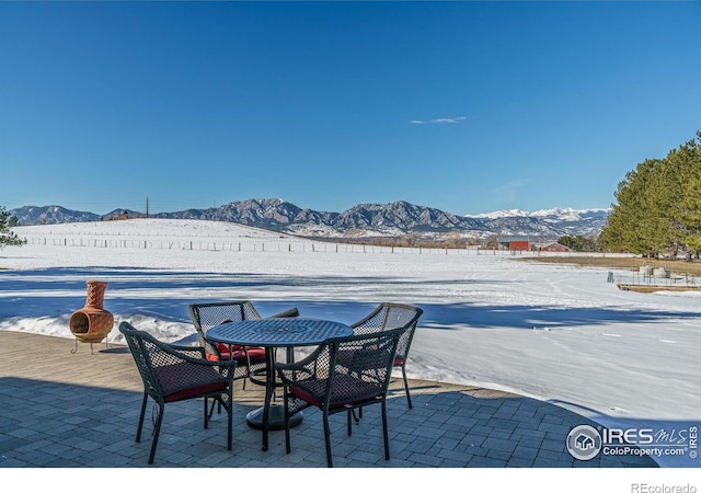 snow covered patio with a mountain view and outdoor dining area