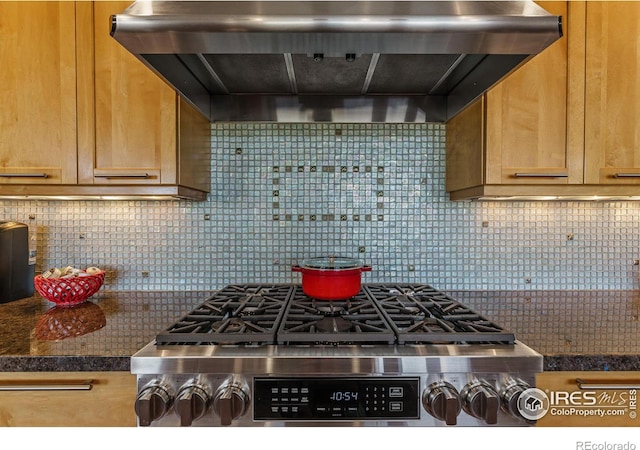 kitchen with dark countertops, decorative backsplash, cooktop, and wall chimney range hood