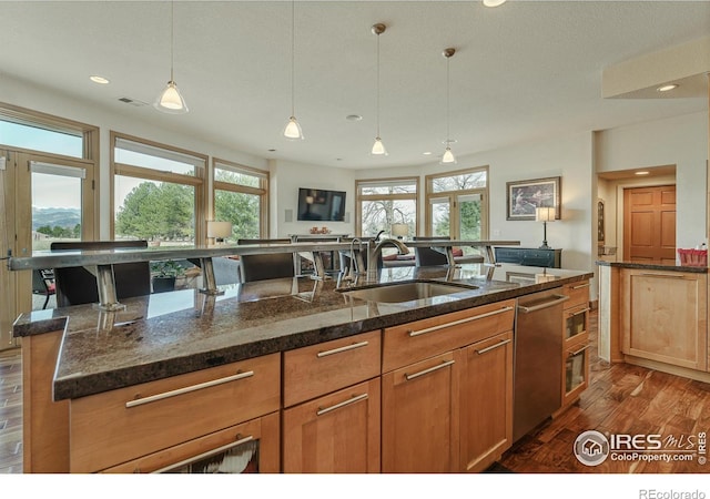 kitchen with a sink, dark stone countertops, dark wood-style flooring, and hanging light fixtures