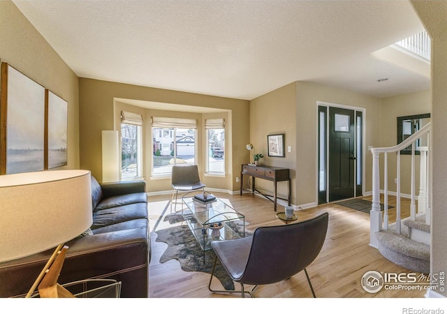 living area with stairway, light wood-style floors, and a textured ceiling