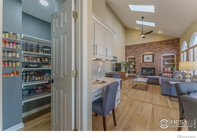 living room featuring light wood finished floors, high vaulted ceiling, a brick fireplace, and a skylight