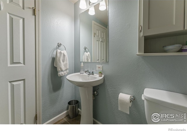 half bath featuring tile patterned floors, baseboards, toilet, and a textured wall