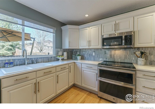 kitchen with backsplash, light countertops, light wood-style flooring, appliances with stainless steel finishes, and a sink