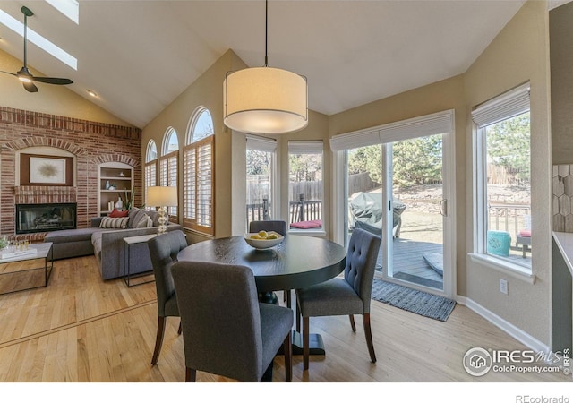 dining space with baseboards, high vaulted ceiling, wood finished floors, and a fireplace