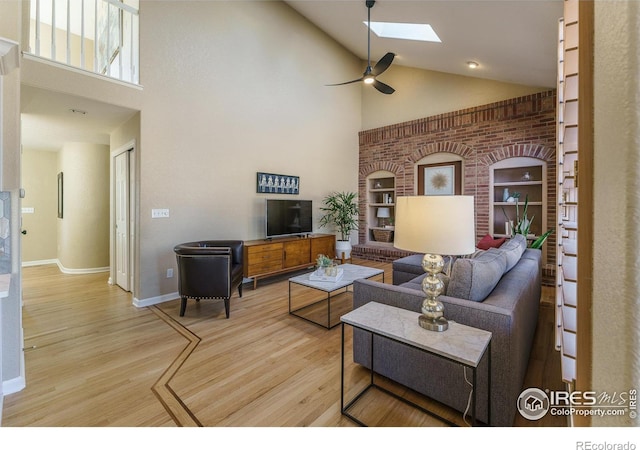 living area featuring ceiling fan, a skylight, wood finished floors, and high vaulted ceiling