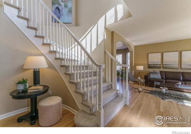 staircase featuring arched walkways, a high ceiling, baseboards, and wood finished floors