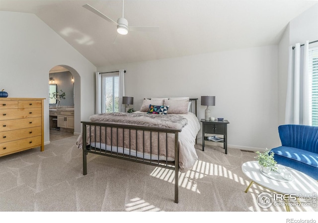 carpeted bedroom with connected bathroom, arched walkways, ceiling fan, and vaulted ceiling