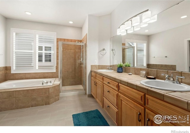 full bath featuring a sink, a stall shower, double vanity, and a bath