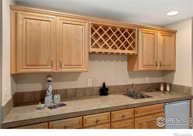 kitchen with dishwashing machine, light brown cabinets, and a sink