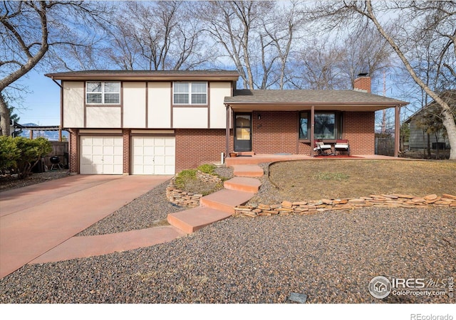 split level home featuring brick siding, an attached garage, stucco siding, a chimney, and driveway