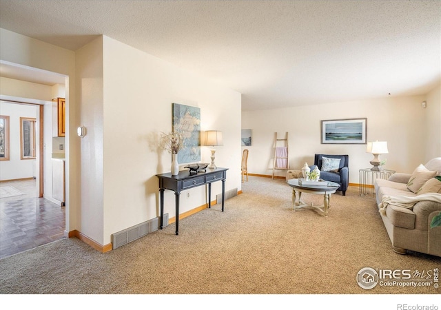 carpeted living area with visible vents, a textured ceiling, and baseboards