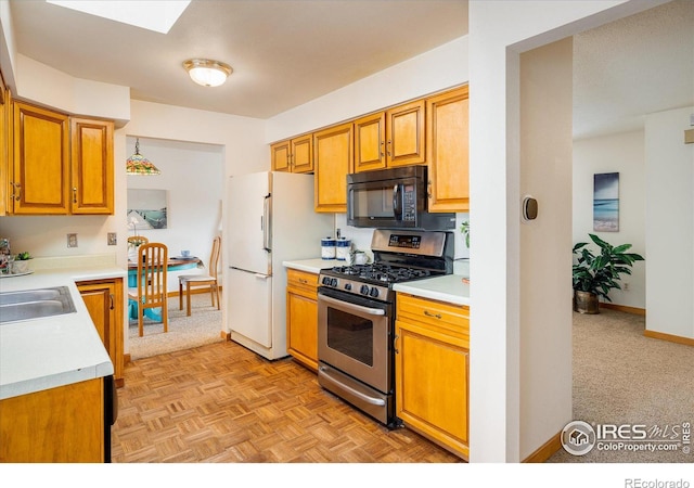 kitchen featuring stainless steel gas range oven, a sink, freestanding refrigerator, black microwave, and light countertops