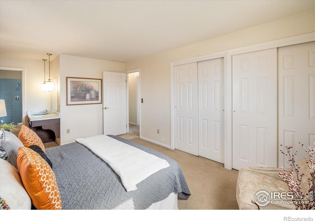 bedroom featuring baseboards, light colored carpet, connected bathroom, and multiple closets