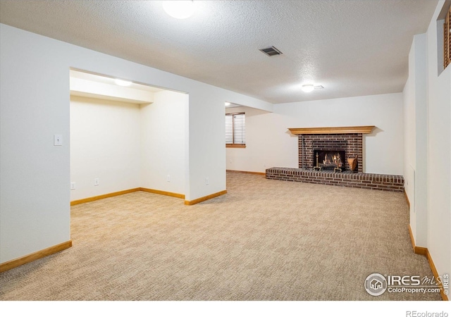 basement featuring visible vents, a fireplace, a textured ceiling, and carpet floors