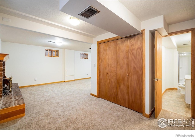 finished below grade area featuring visible vents, light colored carpet, a textured ceiling, and baseboards