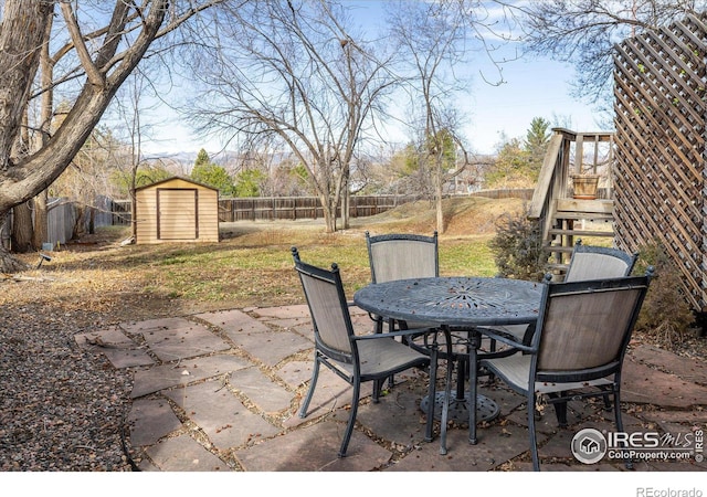 view of patio / terrace featuring a shed, stairs, a fenced backyard, an outbuilding, and outdoor dining space