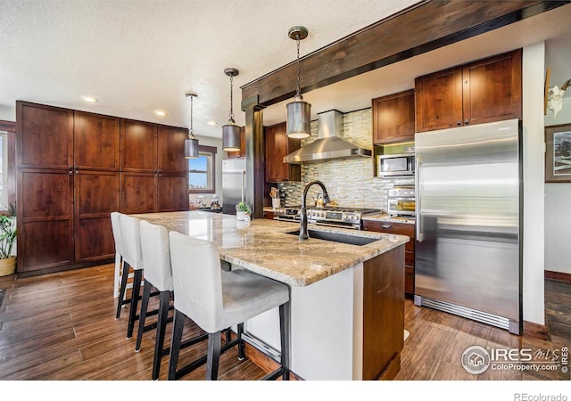 kitchen with light stone counters, stainless steel appliances, decorative backsplash, dark wood-type flooring, and wall chimney exhaust hood