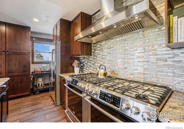 kitchen with backsplash, a textured ceiling, wood finished floors, appliances with stainless steel finishes, and wall chimney exhaust hood