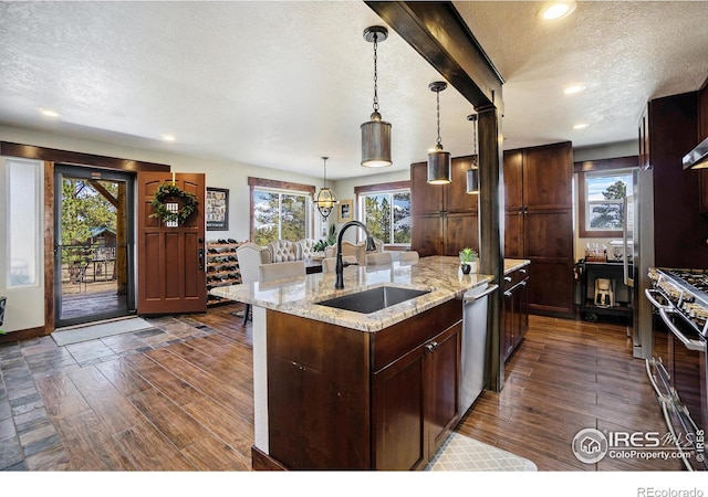 kitchen with an island with sink, a sink, dark wood-type flooring, appliances with stainless steel finishes, and a textured ceiling