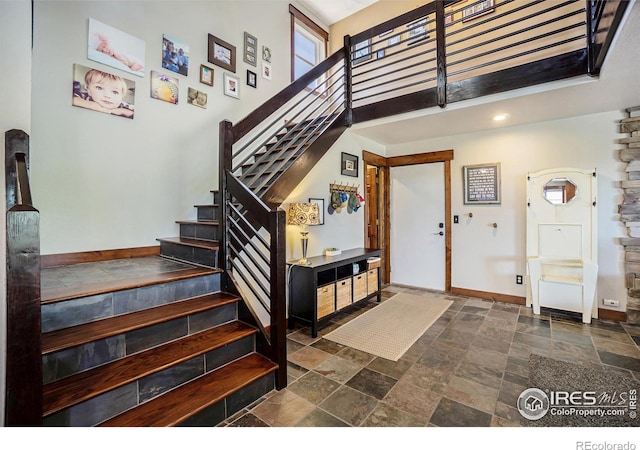 entryway featuring stairs, stone finish floor, baseboards, and a towering ceiling