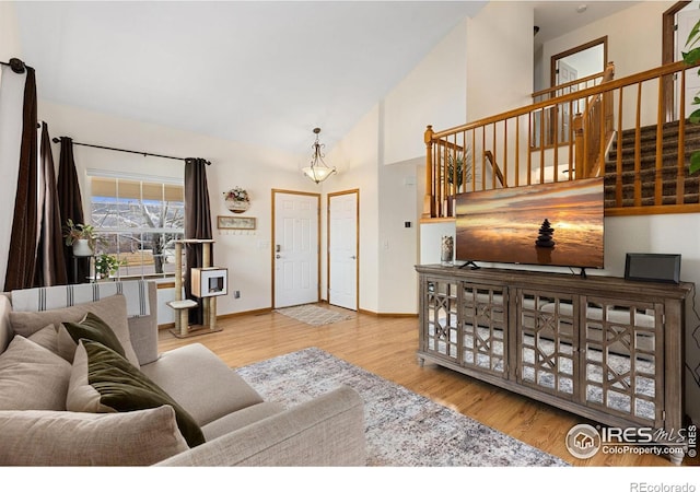 living area featuring baseboards, high vaulted ceiling, wood finished floors, and stairs