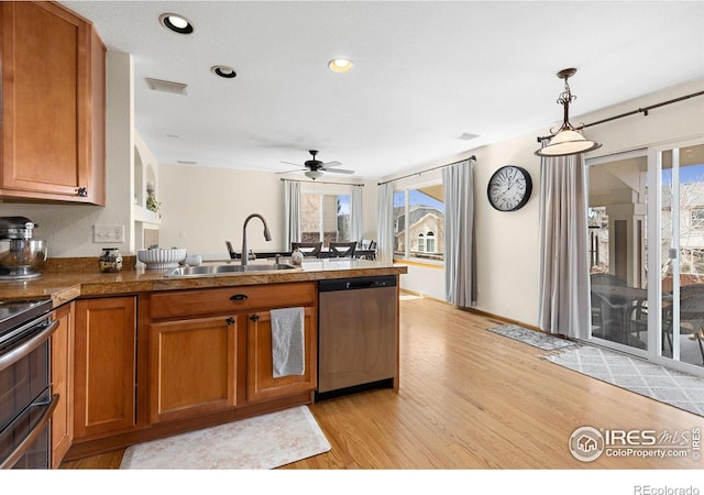 kitchen with brown cabinetry, a peninsula, light wood-style flooring, a sink, and dishwasher