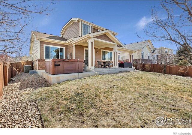 back of house featuring a patio, cooling unit, a fenced backyard, a hot tub, and a lawn