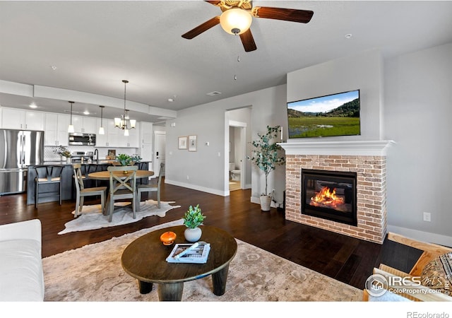 living area with a fireplace, baseboards, ceiling fan, and dark wood-style flooring