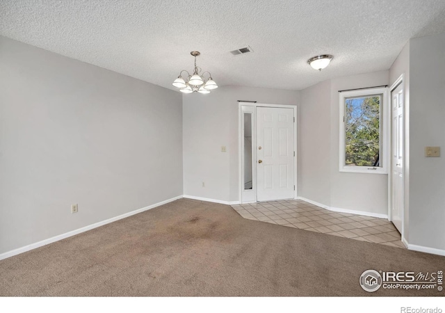 carpeted spare room featuring a notable chandelier, baseboards, visible vents, and a textured ceiling