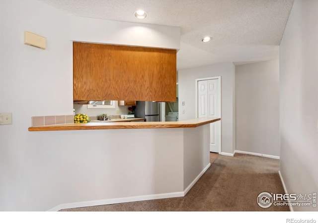 kitchen featuring baseboards, carpet floors, washer / dryer, freestanding refrigerator, and a textured ceiling