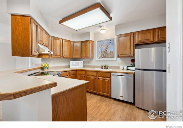 kitchen featuring brown cabinets, under cabinet range hood, stainless steel appliances, a peninsula, and light countertops