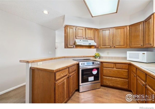 kitchen with white microwave, under cabinet range hood, stainless steel electric range oven, brown cabinets, and a peninsula