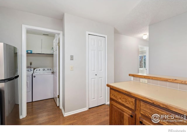 kitchen featuring brown cabinets, washer and clothes dryer, wood finished floors, freestanding refrigerator, and light countertops