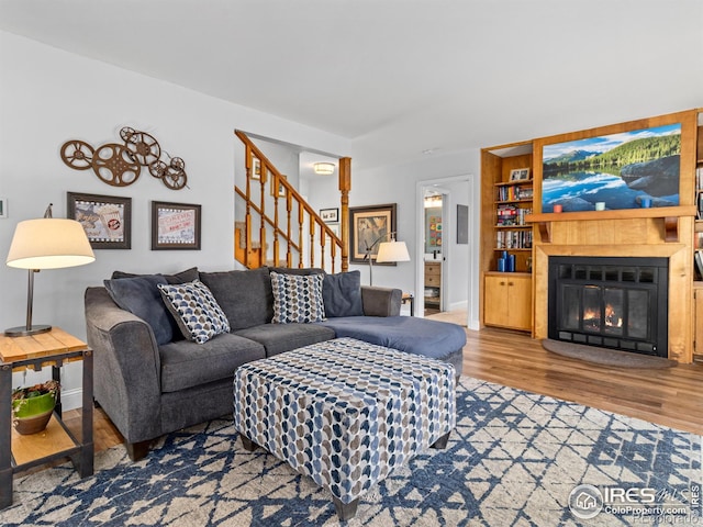 living room with built in features, a glass covered fireplace, wood finished floors, stairway, and baseboards