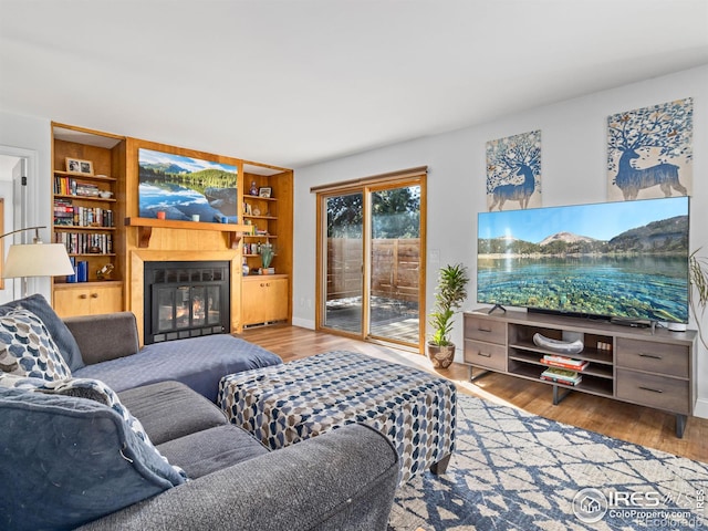 living room with a glass covered fireplace, built in features, baseboards, and wood finished floors