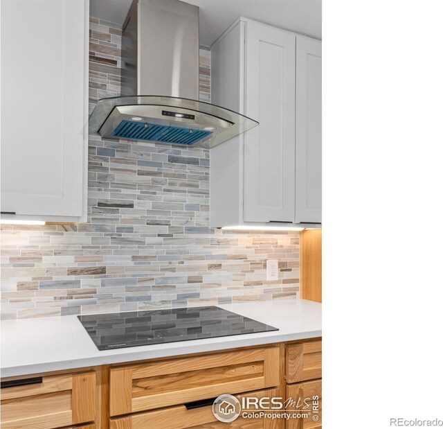 kitchen featuring light countertops, white cabinets, black electric stovetop, wall chimney exhaust hood, and backsplash