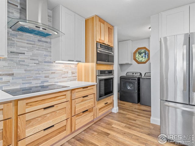 kitchen featuring light wood finished floors, backsplash, washing machine and dryer, appliances with stainless steel finishes, and wall chimney exhaust hood