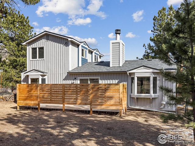 rear view of property with board and batten siding, a shingled roof, a chimney, and fence