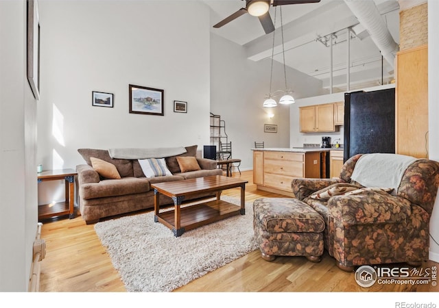 living room with light wood finished floors, a high ceiling, and a ceiling fan