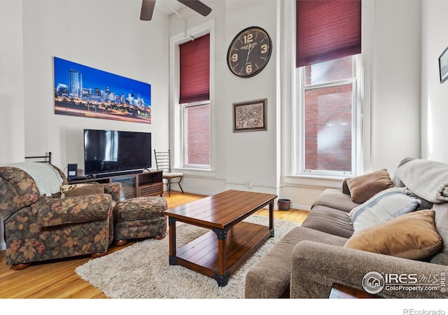 living room featuring baseboards, a high ceiling, wood finished floors, and a ceiling fan