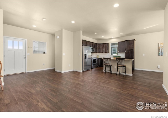 3948 Hackberry St, Wellington, CO 80549 - kitchen with dark brown cabinetry, a kitchen bar, decorative backsplash, appliances with stainless steel finishes, and dark wood-style floors
